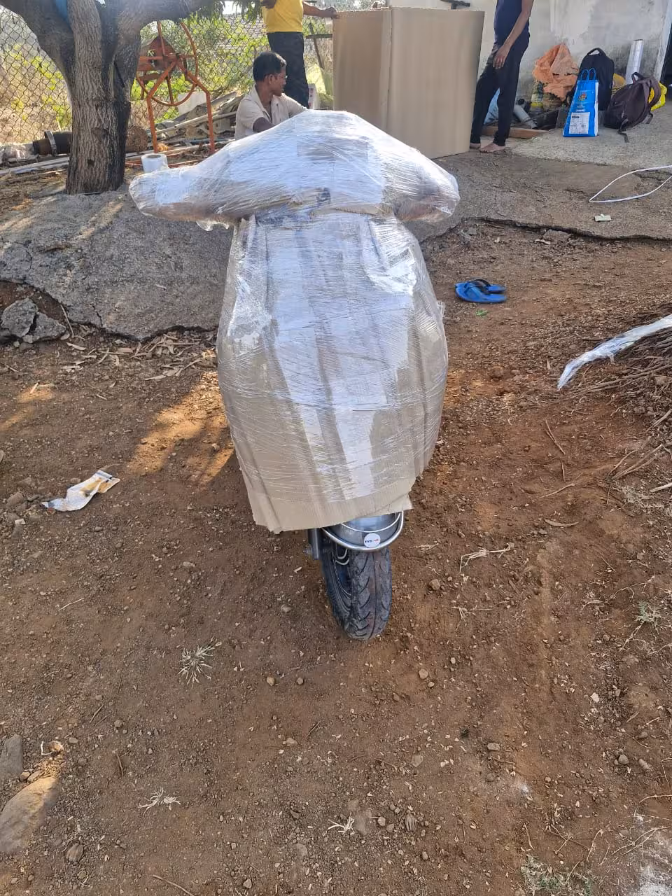 A scooter fully wrapped in protective brown paper and clear plastic for transport, viewed from the front.