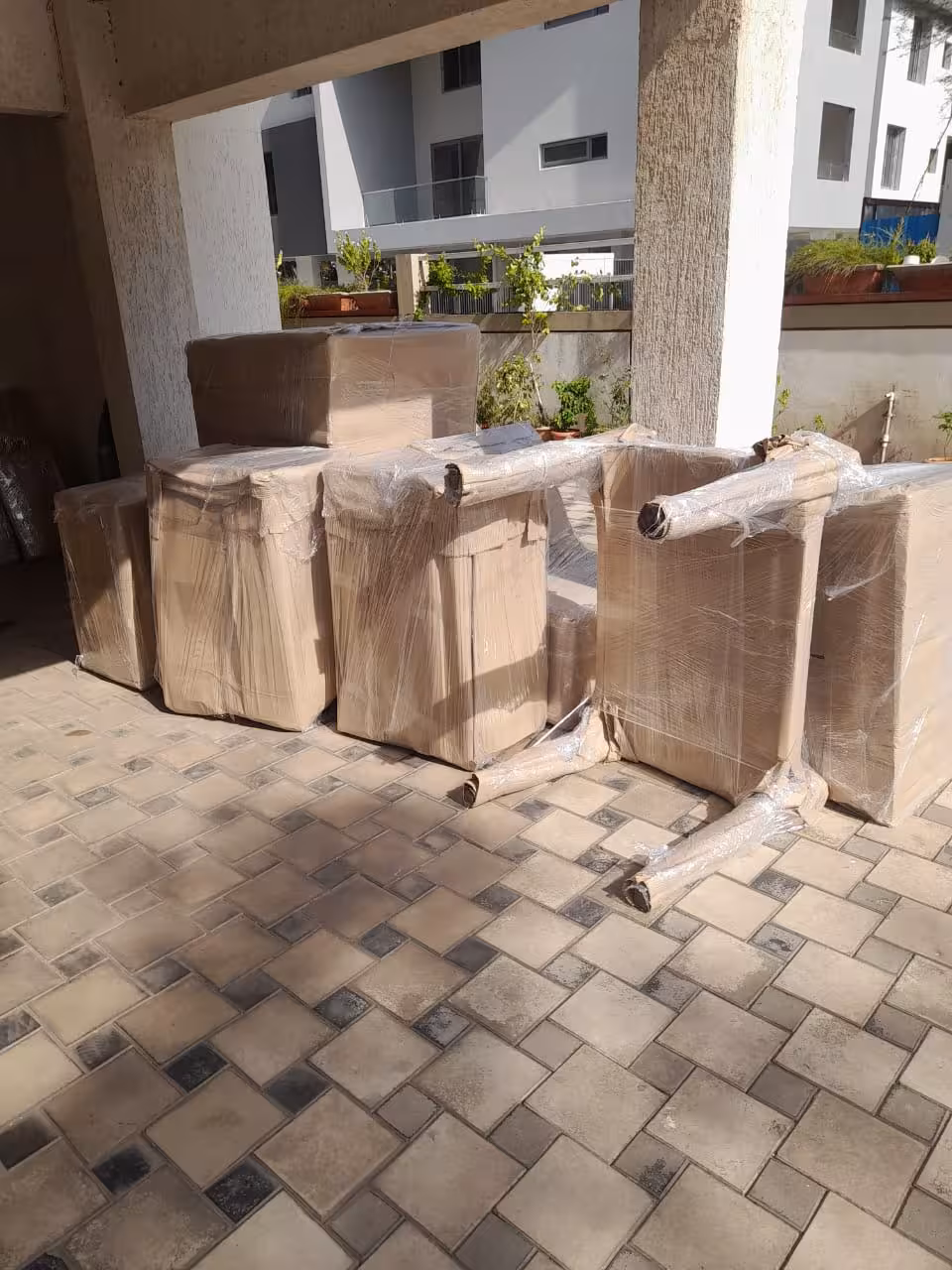 A group of large, wrapped furniture items placed on a paved outdoor area, ready for transport