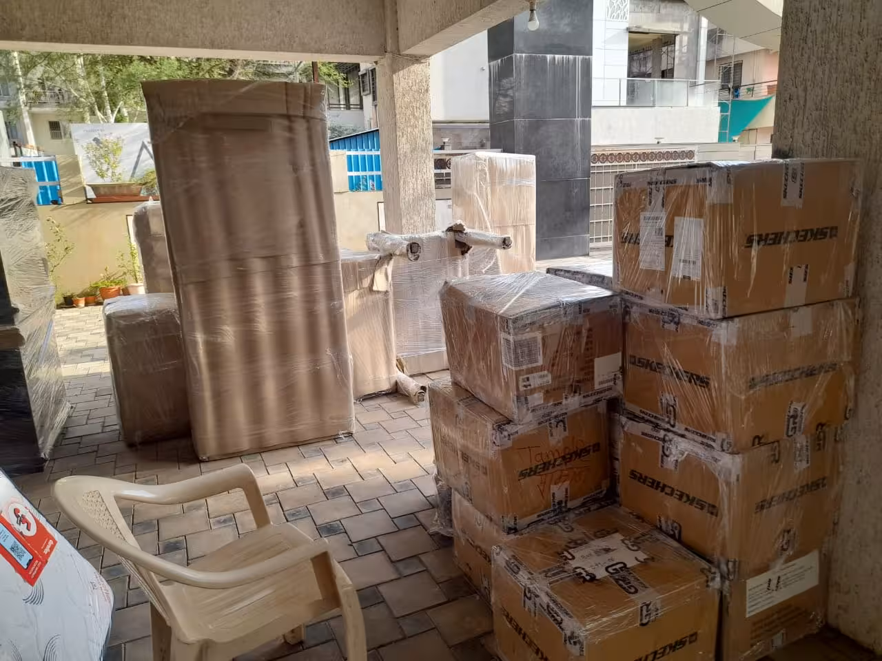 Numerous packed cardboard boxes, some labeled 'SKECHERS', and wrapped furniture items in an outdoor loading area