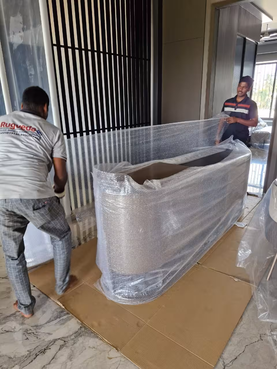 Movers carefully wrapping a long, curved piece of furniture in bubble wrap