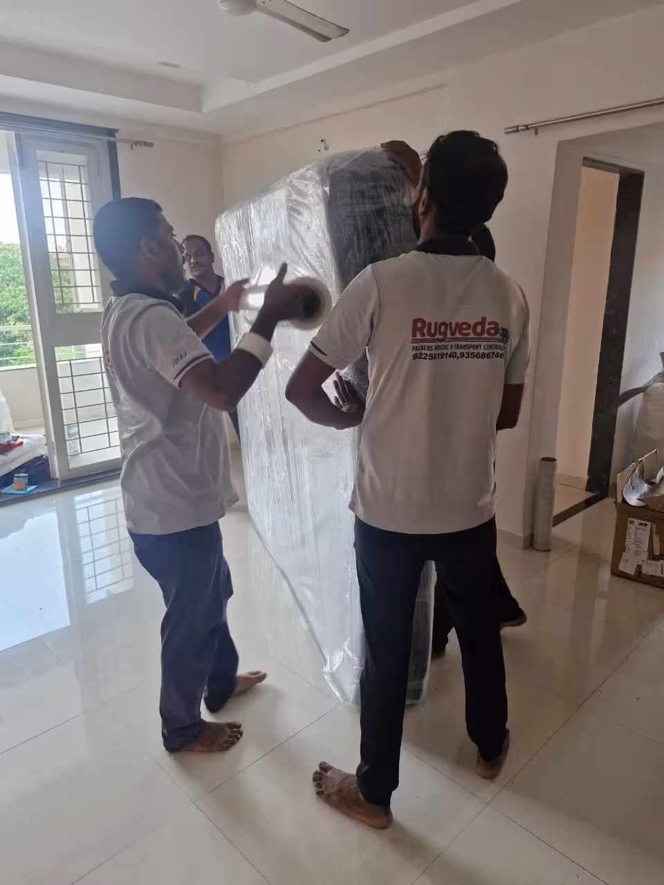 Two movers wrapping a large, square item with plastic film