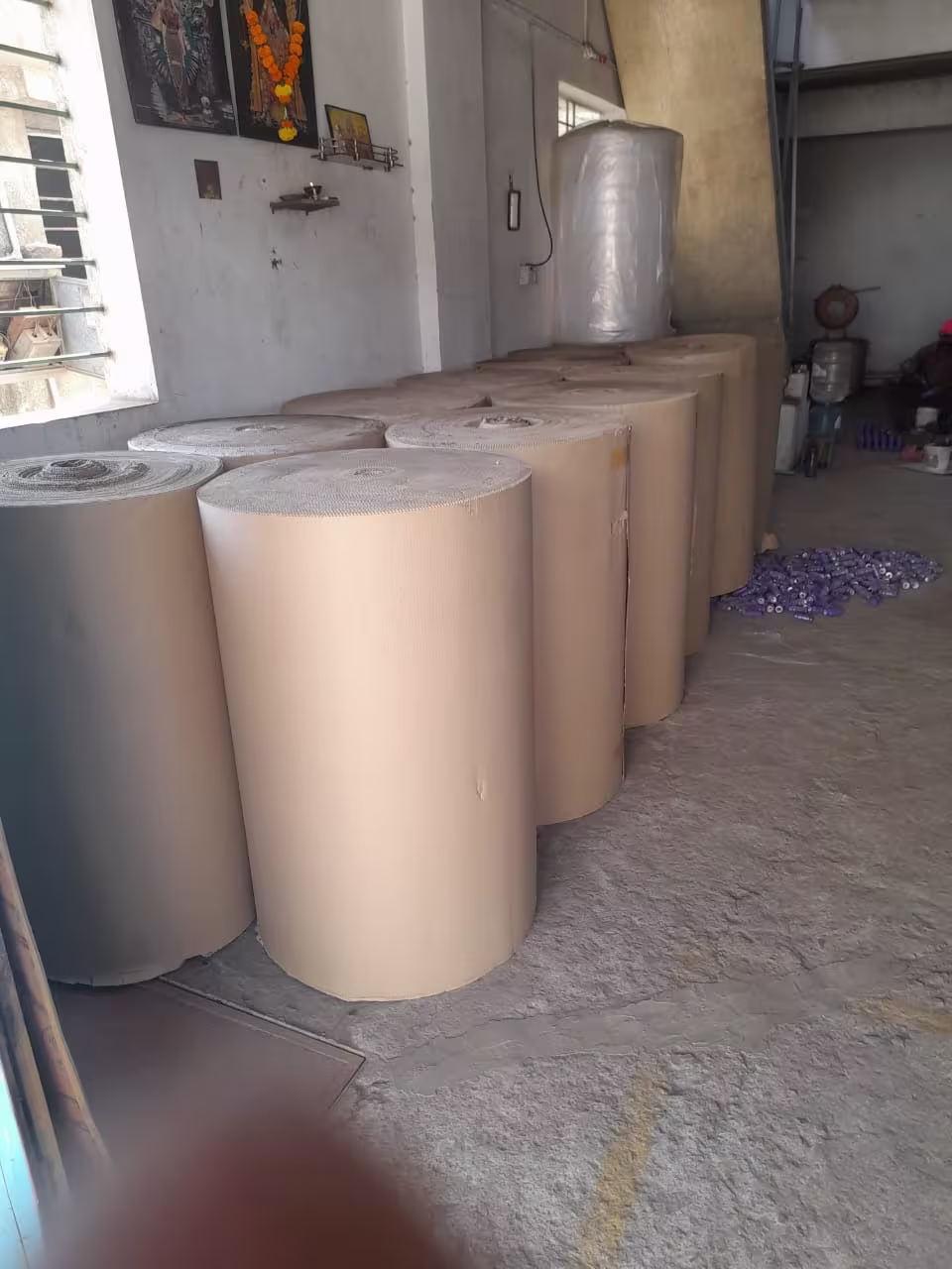 Large rolls of brown corrugated cardboard and clear plastic wrap in a warehouse or storage facility.